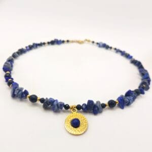 Ręcznie wykonany naszyjnik marki Witchhouse z surowych bryłek lapis lazuli i czarnego onyksu, ozdobiony złotą zawieszką w formie teksturowanej rozety z niebieskim oczkiem.