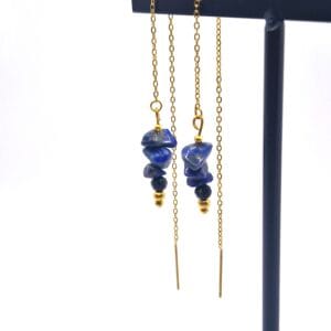 Kolczyki w kolorze złotym przeciągane ozdobione surowymi bryłkami niebieskiego lapis lazuli oraz fasetowanym czarnym onyksem na cienkim łańcuszku.