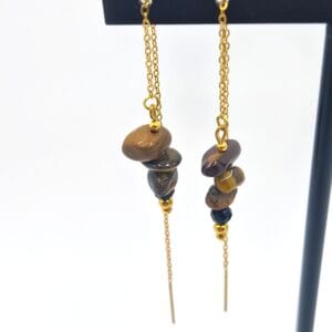 Kolczyki w kolorze złotym przeciągane z gładkimi bryłkami brązowego tygrysiego oka oraz fasetowanym czarnym onyksem na cienkim łańcuszku.