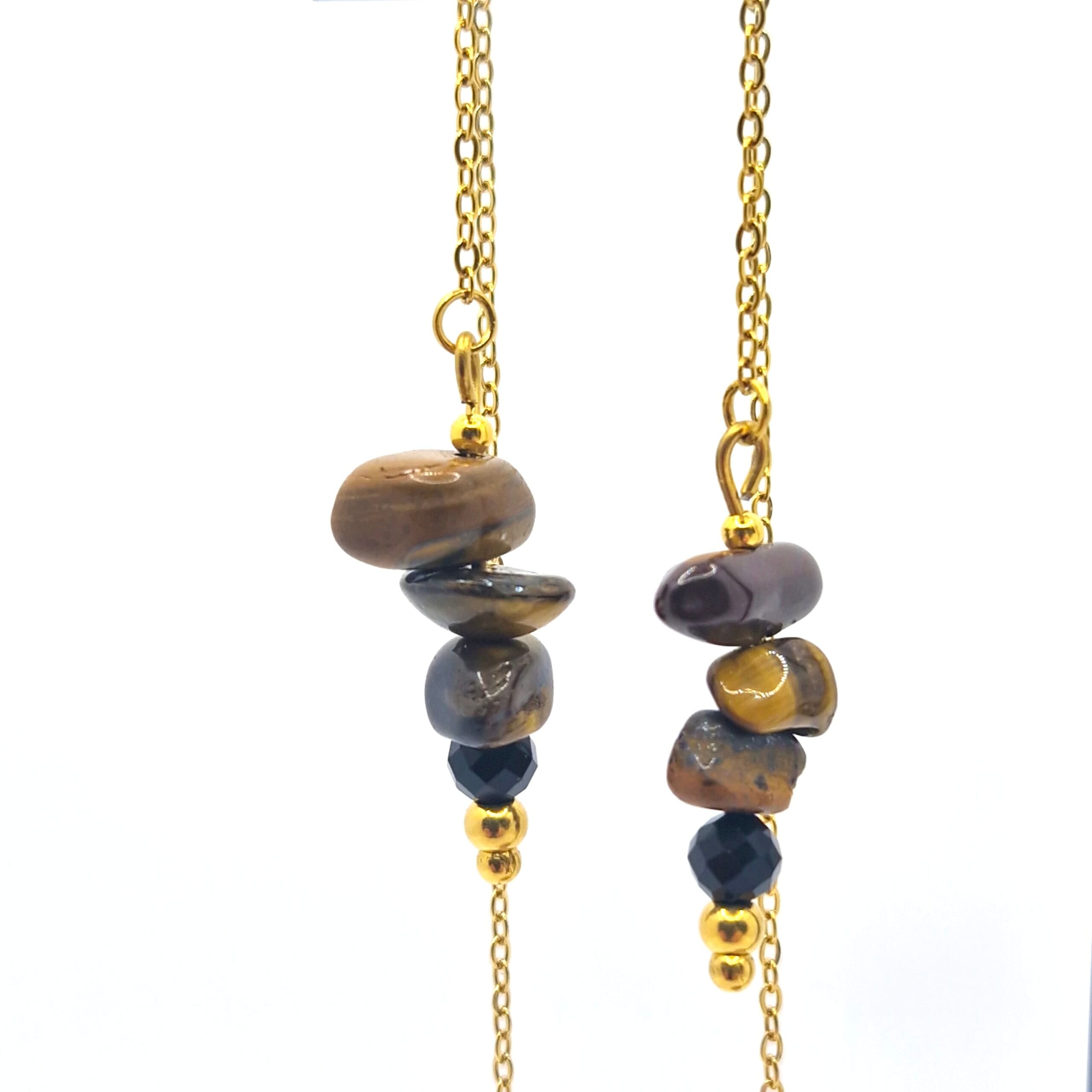 Zbliżenie na naturalne, brązowe bryłki tygrysiego oka oraz fasetowany czarny onyks w oprawie ze złoconej stali.